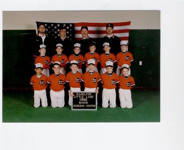 Youth baseball team in orange jerseys with US flag.
