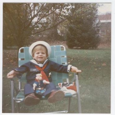 Toddler in sailor outfit sitting outside.