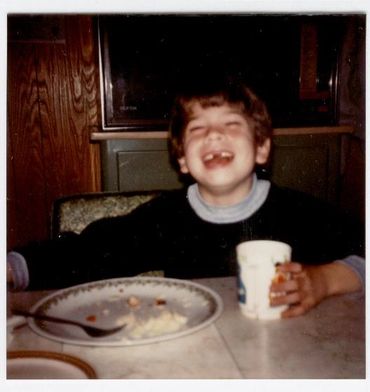 Young boy laughing at dinner table.