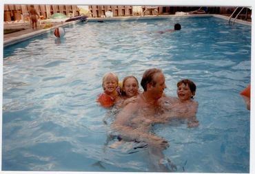Children playing with an adult in pool.