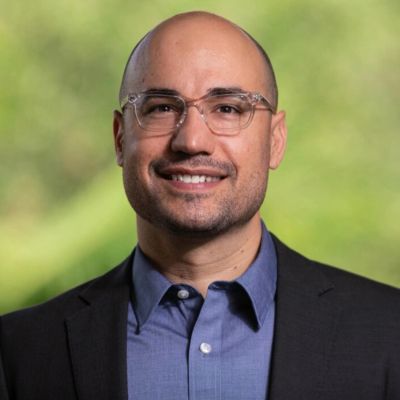 Smiling man wearing glasses, a blue shirt, and a black blazer.