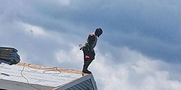 Person standing precariously on a rooftop edge under a cloudy sky.