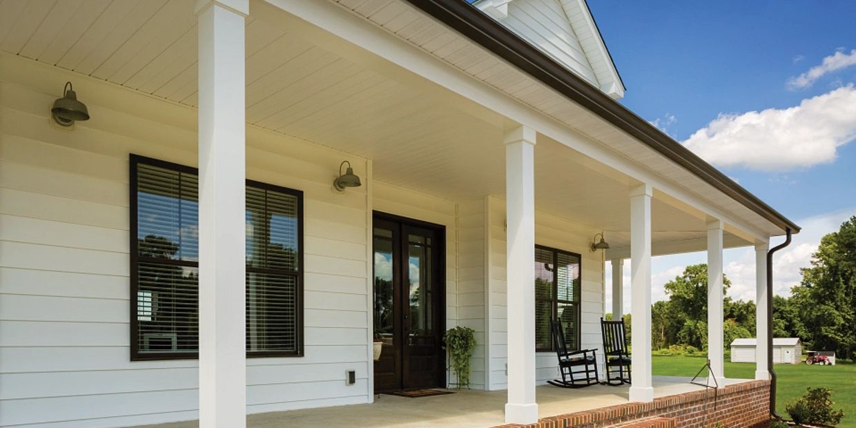 A white house porch with rocking chairs and potted plant under a clear sky.