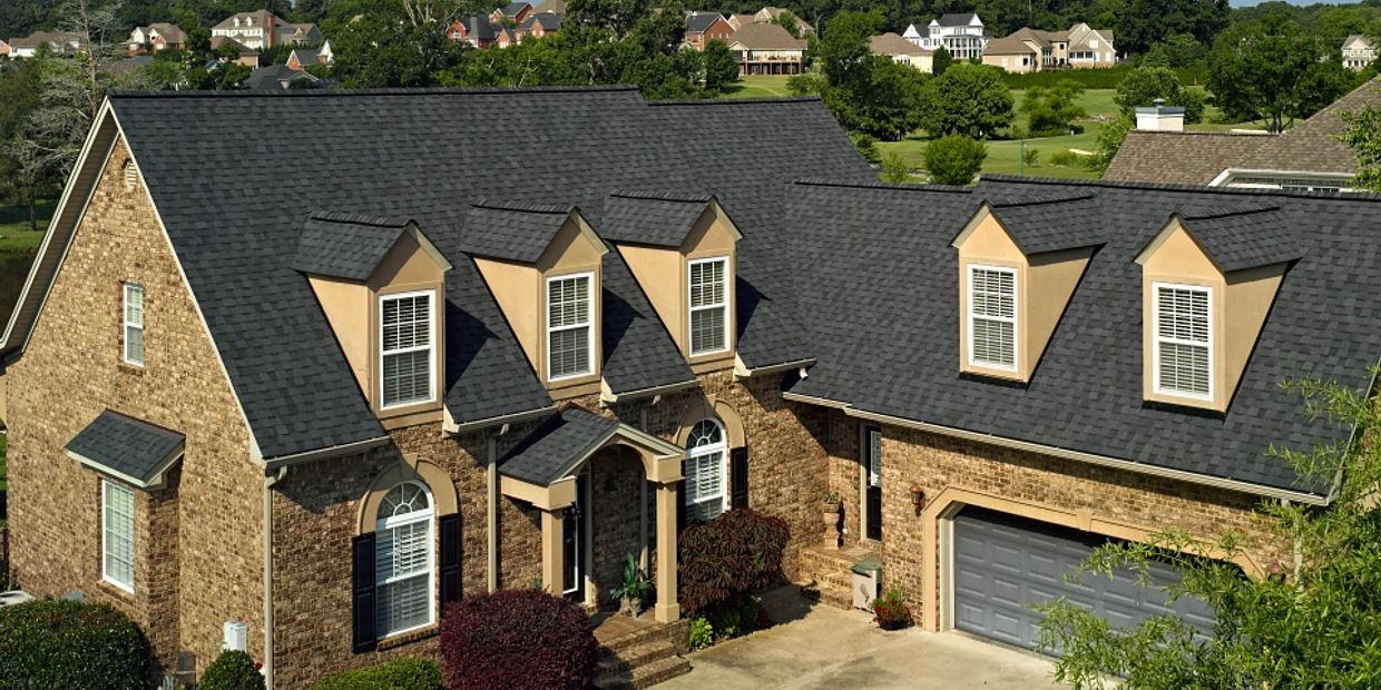 Elegant brick house with dark shingle roof and multiple dormer windows.