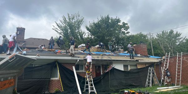 Workers repair a large roof under cloudy skies.