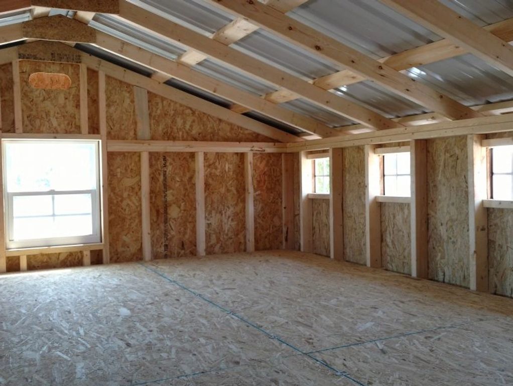 Interior view of an unfinished wooden structure with windows and metal roof panels.