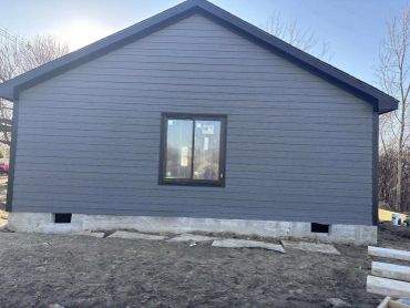 Gray house exterior with a single window and concrete foundation.