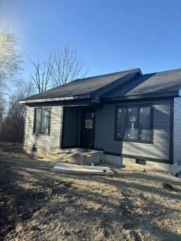 Small gray house under construction on a clear day.