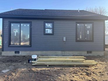 Newly constructed house with dark siding and windows still covered with protective film.