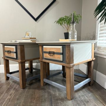 Two wooden side tables with drawers in a corner room.