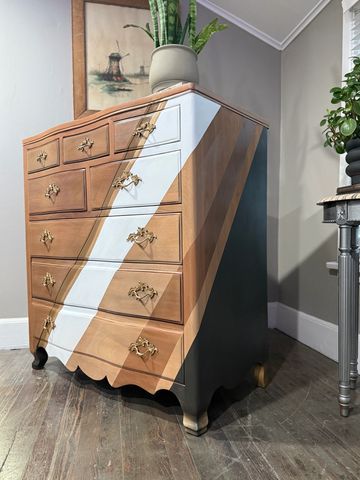 A wooden chest of drawers with a white diagonal stripe and a potted plant on top.