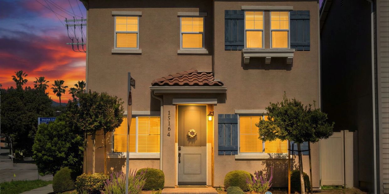 A cozy house at sunset with warm lights glowing from windows.
