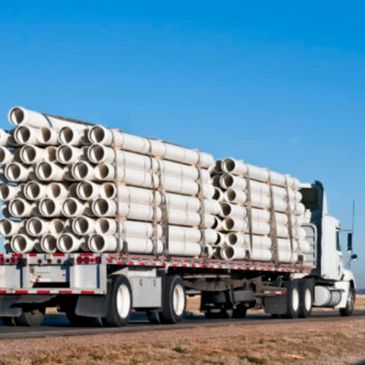 Truck loaded with stacked white pipes.