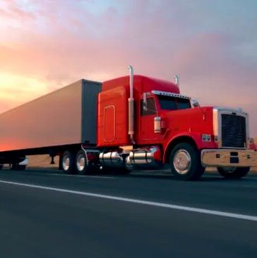 Red semi-truck driving on highway at sunset.