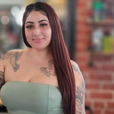 Woman with long hair and tattoos wearing a strapless top.