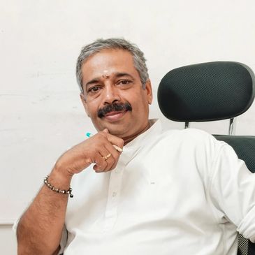 Middle-aged man with gray hair and mustache sitting in a black chair, wearing a white shirt.
