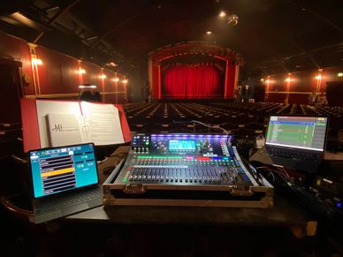 Audio mixing setup in an empty theater with red curtains and dim lights.