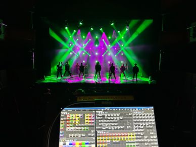 Silhouetted performers on stage under vibrant green and purple lights.