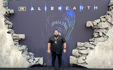 Man standing in front of an Alien Earth FX promotional backdrop with cracked wall design.