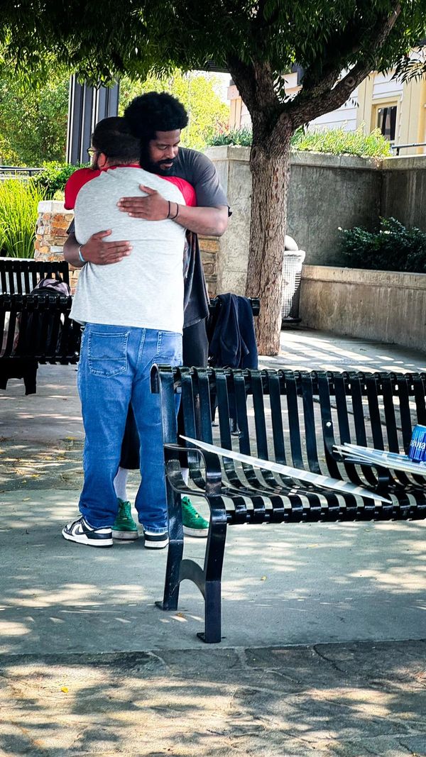 Two men sharing a warm hug in a park under a tree.