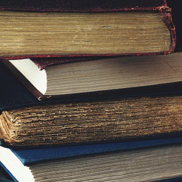 A stack of old, worn books with thick pages and frayed edges.