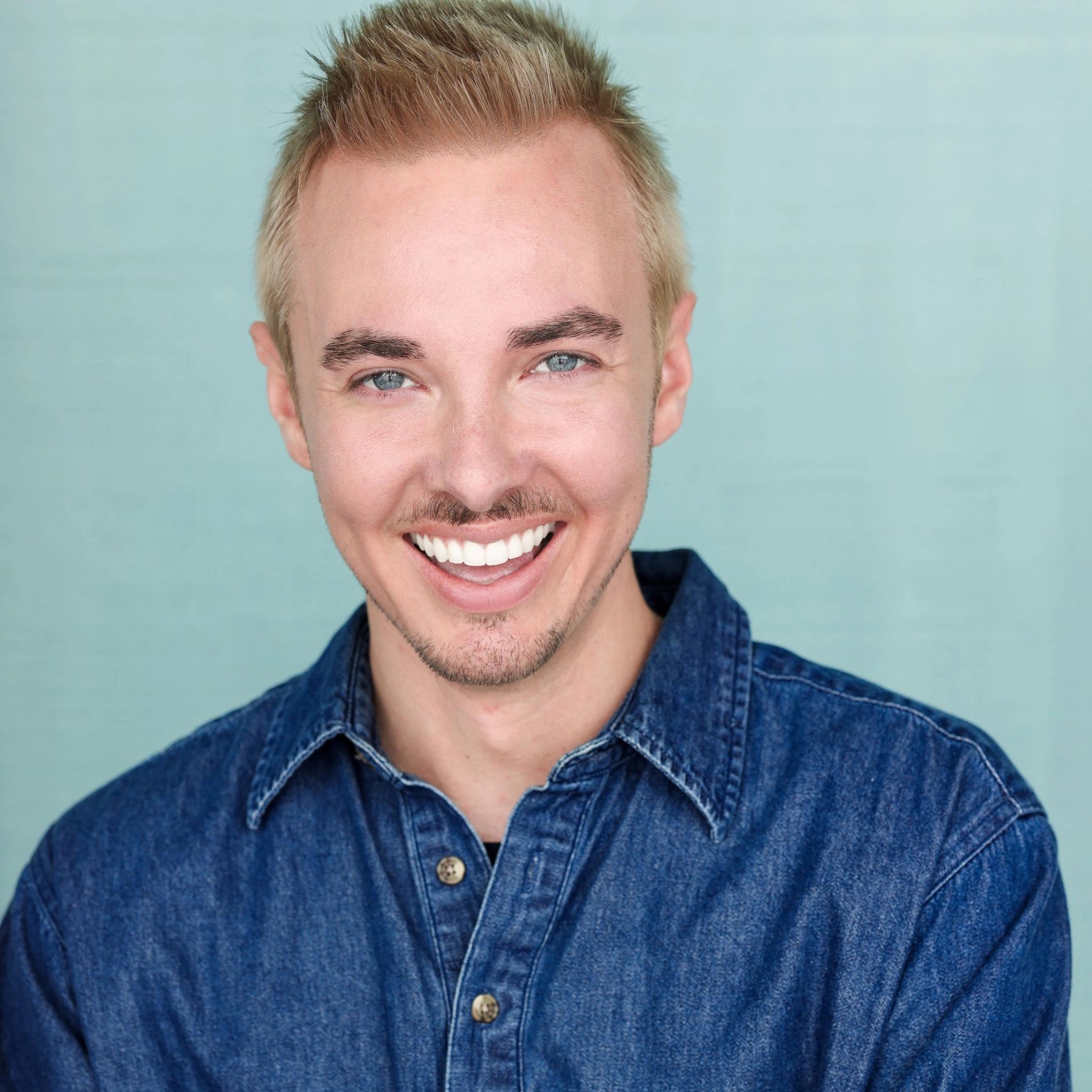 Smiling man with blue eyes wearing a denim shirt.