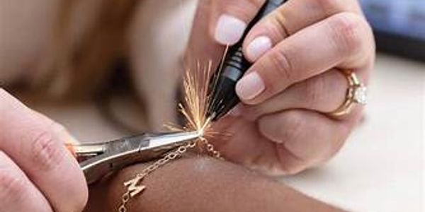 Close-up of hands engraving a metal bracelet with a tool.