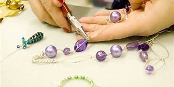 Hands crafting purple bead jewelry using pliers.