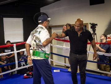 Two men fist bump in a boxing ring with spectators around.