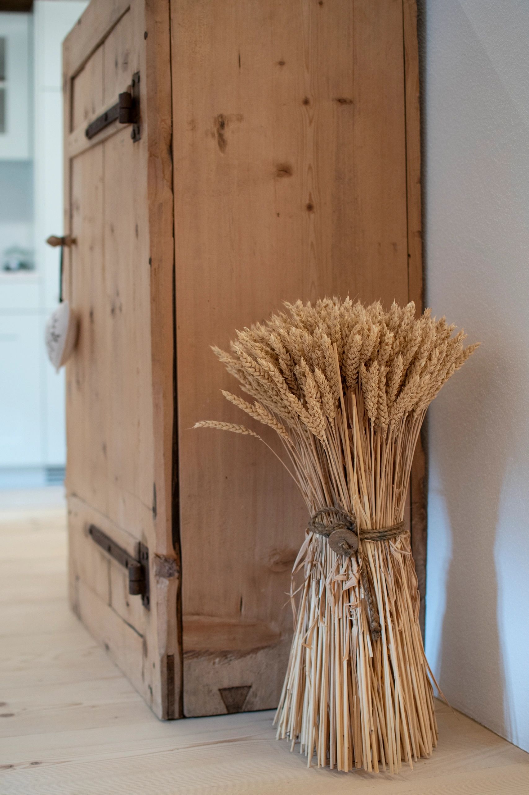 Bundle of dried wheat stalks tied with twine next to a rustic wooden cabinet.
