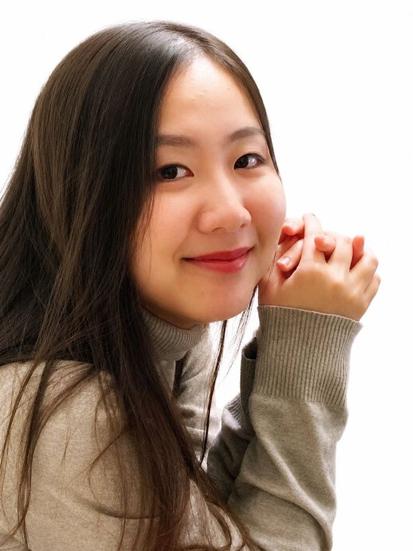 Young woman with long hair smiling gently, wearing a beige sweater.