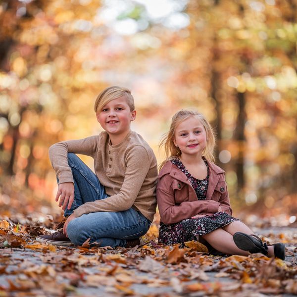 Two children sitting on a leaf-covered path during autumn.
