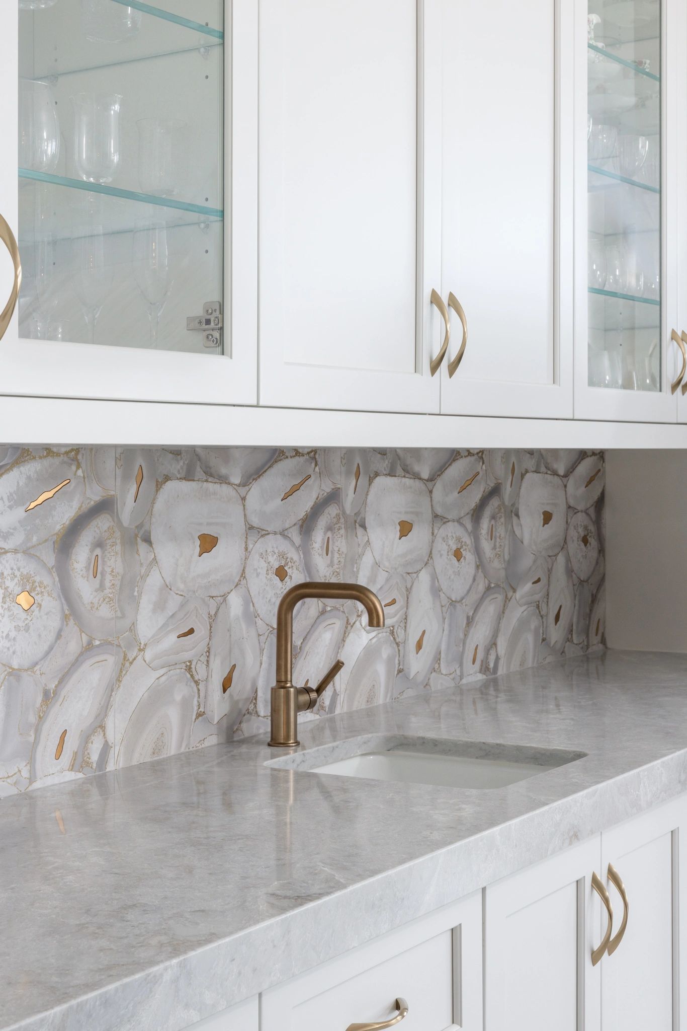 Elegant white kitchen with marble countertop and gold faucet.