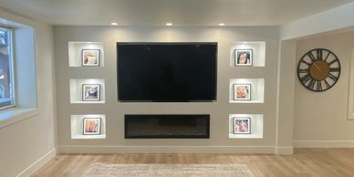 Modern living room wall with TV, fireplace, and illuminated photo frames.