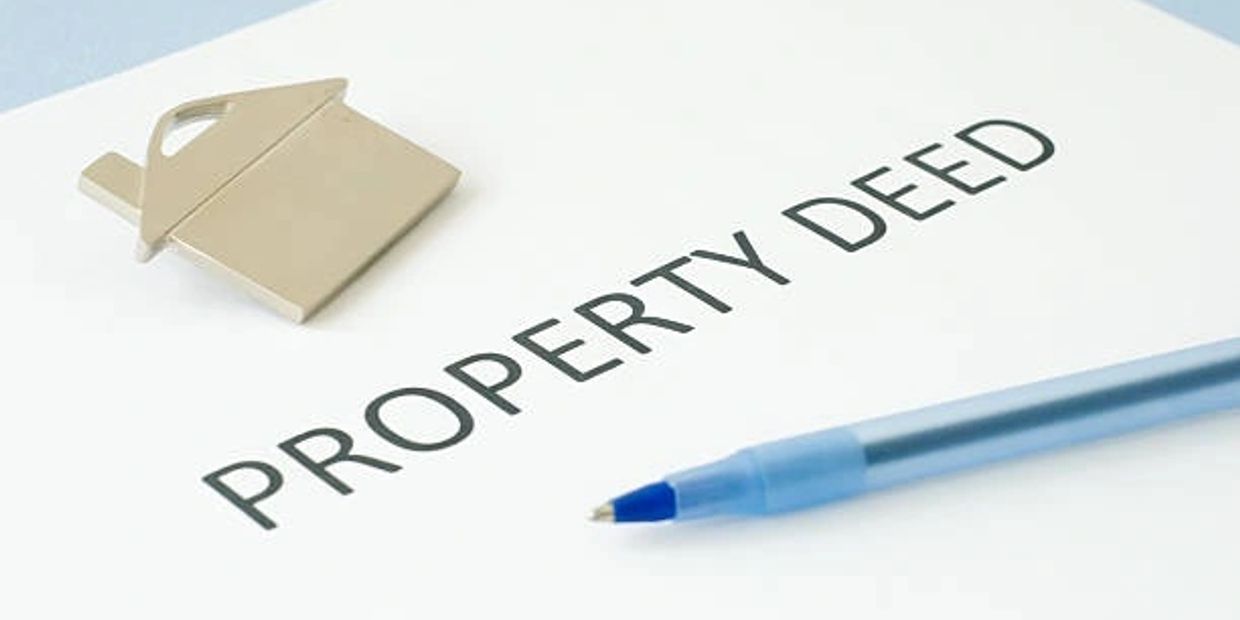 Property deed document with a pen and house-shaped paperclip.