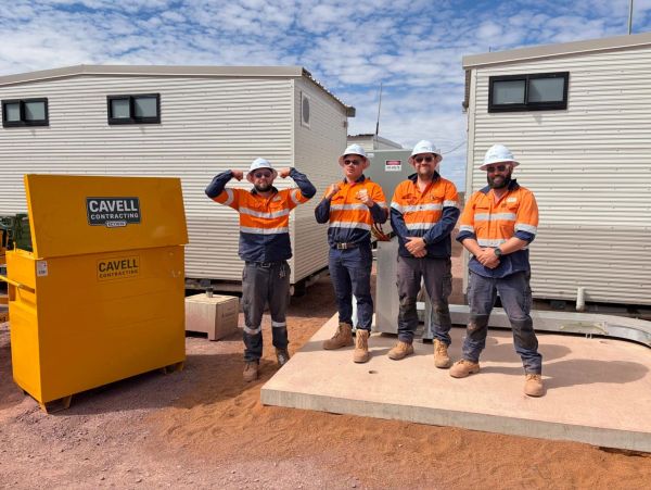Four construction workers in orange and navy uniforms standing outdoors.