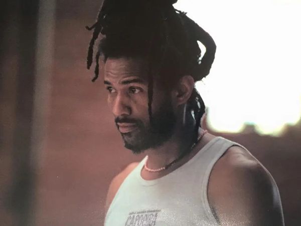 Man with dreadlocks wearing a white tank top and necklace.