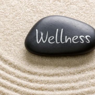 A black stone with 'Wellness' inscribed, placed on raked sand.