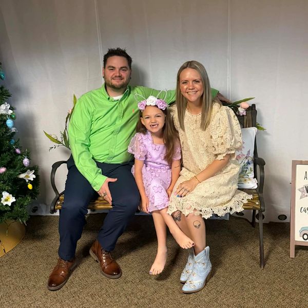 A happy family of three sitting on a bench, smiling at the camera.