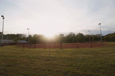 Sunset over a fenced circular area in a grassy field.