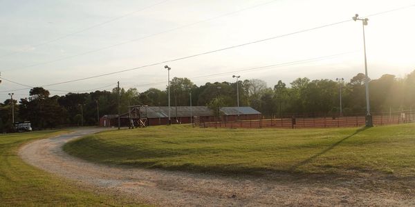 I’m A rural sports field with a dirt road curving beside it during sunset.