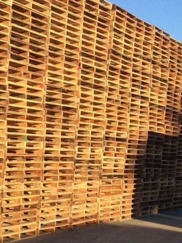 A large stack of wooden pallets arranged outdoors under sunlight.