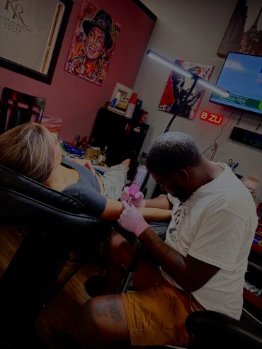 Tattoo artist working on a client's arm in a studio.