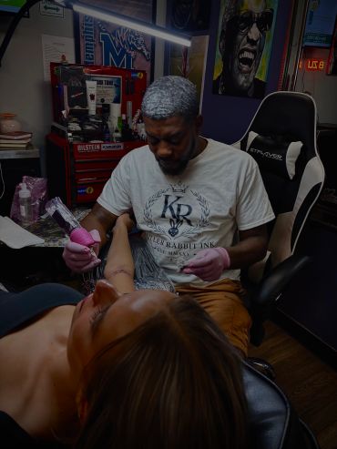 Tattoo artist working on a woman's arm in a studio.