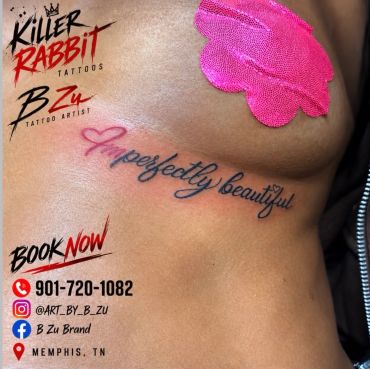 Tattoo saying 'Imperfectly beautiful' on ribcage with tattoo artist details.