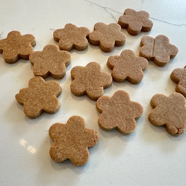 Flower-shaped brown dough cookies on a white surface.