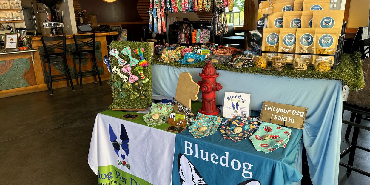 A pet-themed vendor table with bandanas, treats, and accessories inside a cozy shop.