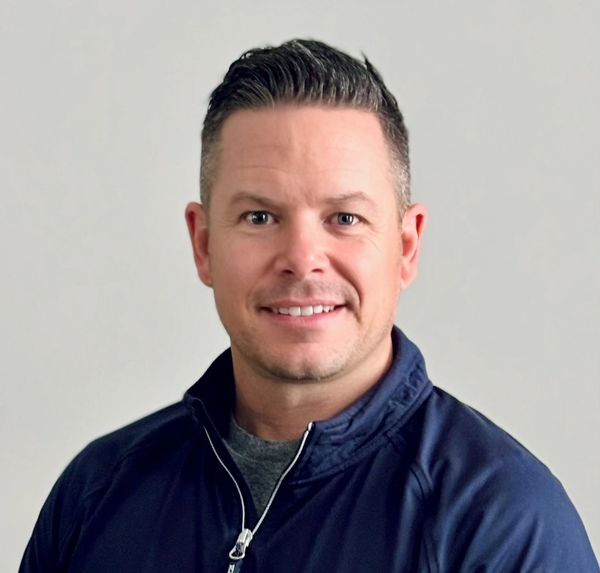 Smiling man in a navy blue jacket against a plain background.