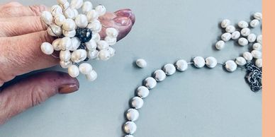 Woman with multi pearl ring on finger and silver beaded necklace on table with light blue background