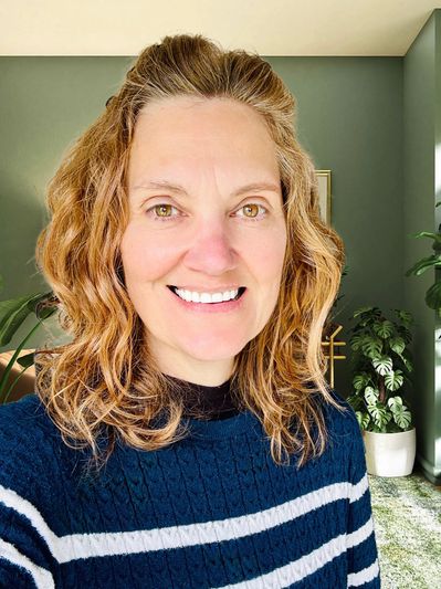 Smiling woman with curly hair in a striped sweater indoors.